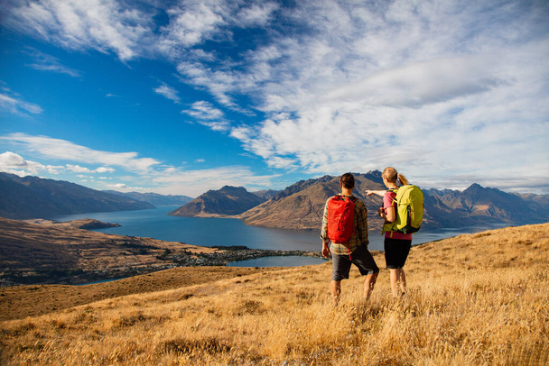 Jong Nieuw-Zeeland reizen toeristisch paar met rugzakken ontspannen bekijken The Remarkables op vakantie in de buurt van Lake Wakatipu Otago - Foto, afbeelding