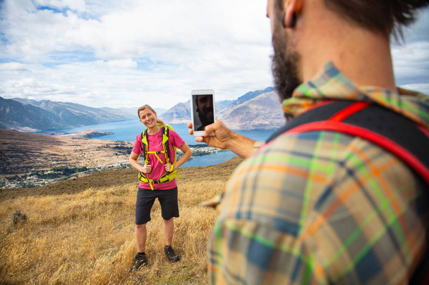 Queenstown viaggio caucasico giovane maschio utilizzando la tecnologia smartphone scattare foto della sua ragazza raggiungendo le sue ambizioni escursioni di Fjordland Nuova Zelanda  - Foto, immagini