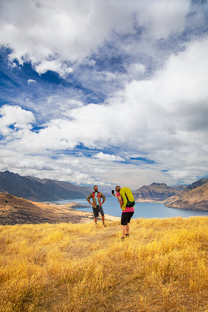 Blanke vrouw met behulp van smartphone-technologie het nemen van foto van haar vriend het bereiken van zijn doelen wandelen in The Remarkables Queenstown reizen Nieuw-Zeeland - Foto, afbeelding