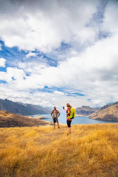 Jonge blanke vrouwelijke reiziger het nemen van een smart phone foto van mannelijke vriend genieten trekking van Wilderness gebied in de buurt van Lake Wakatipu Queenstown Nieuw-Zeeland - Foto, afbeelding