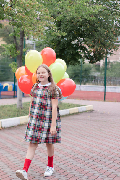 encantadora adolescente em vestido marrom xadrez com um monte de balões coloridos. Menina da escola. muito tween. - Foto, Imagem