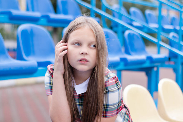 chica bonita en uniforme de vestido de escuela en el tribuno azul y amarillo del estadio de la escuela. Hora de la escuela. tween - Foto, imagen