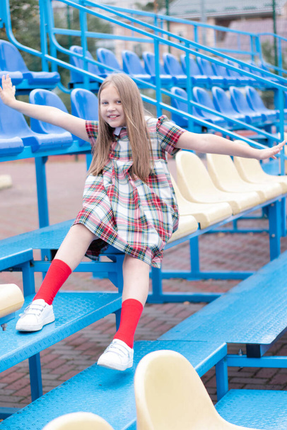 pretty girl in school dress uniform on the blue and yellow tribune of the school stadium. school time. tween - Foto, imagen