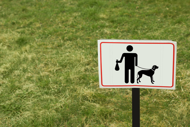 Sign board PLEASE CLEAN UP AFTER YOUR DOGS on green lawn - Photo, image