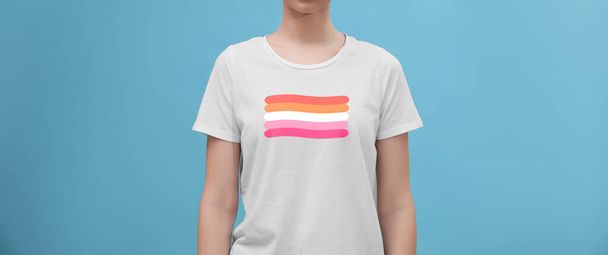 Young woman wearing white t-shirt with lesbian flag on light blue background, banner design. LGBT concept - Фото, изображение