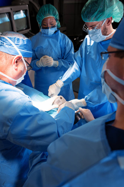 Equipe medica specialistica in prima linea nel teatro ospedaliero con equipaggiamento protettivo individuale operante su pazienti con strumenti chirurgici sterili - Foto, immagini