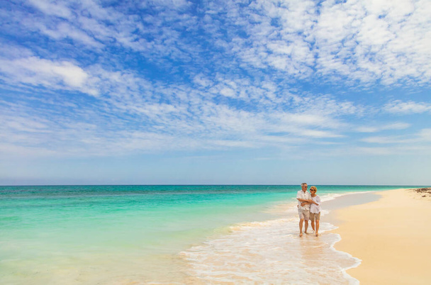 Opuszczona tropikalna wyspa z czułą starszą kaukaską parą spacerującą razem po oceanicznych falach na białej, piaszczystej plaży Bahamy - Zdjęcie, obraz