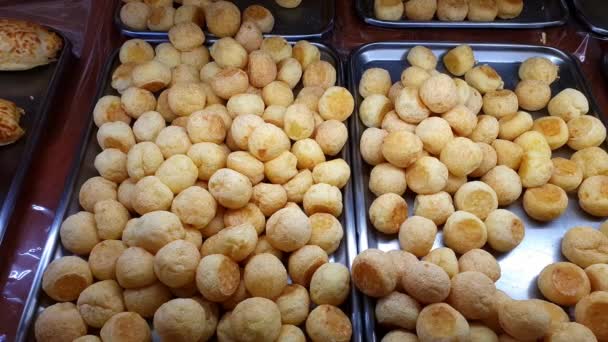 Several cheese puffs being displayed at a Brazilian bakery showcase. - Video