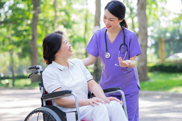 Asian female nurse taking care of a middle-aged female patient in the park - Photo, Image