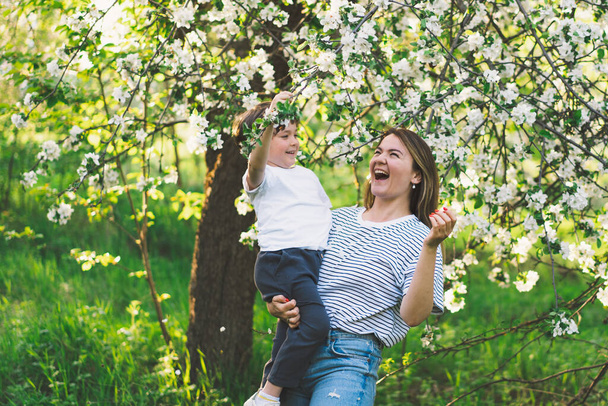 Feliz día de las madres. Madre con su pequeño hijo en el jardín de primavera durante la hora dorada. Madre e hijo - Foto, imagen