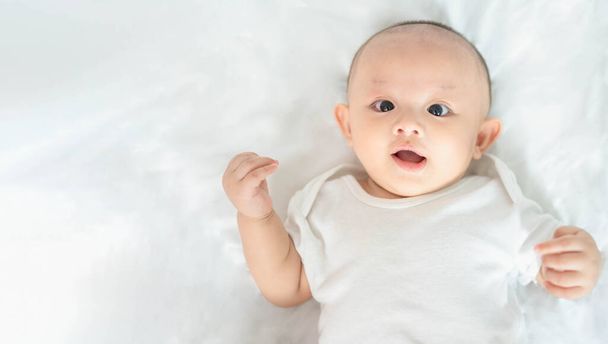 Boldog család, aranyos ázsiai újszülött fiú játszik a fehér ágyon nézz a kamerába nevető mosollyal boldog arccal. Kis ártatlan, új csecsemő imádnivaló gyermek az élet első napján. Anyák napi koncepció. - Fotó, kép