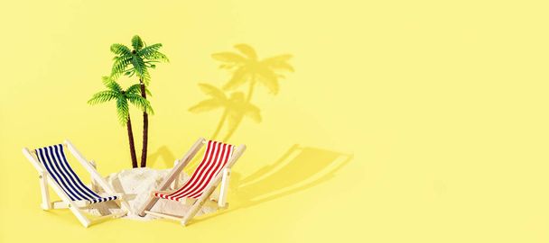 Toy beach deck chairs and palm tree with sand on yellow background. Creative summer beach concept. - Photo, Image