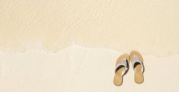 Pare of white sandals on wet sand by sea side, top view with copy space, summer concept  - Photo, Image
