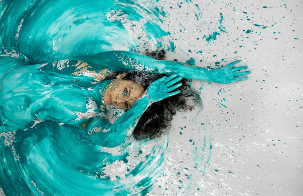 Visão superior de uma mulher nua sexy pintada abstrata verde e branca turquesa, deitada no chão no estúdio azul, pintura de arte corporal abstrata, espaço de cópia - Foto, Imagem