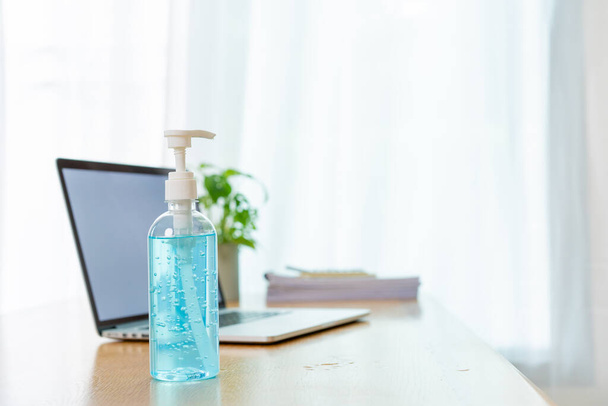 Bottle of liquid hand sanitizer on the wooden table in office, prevention from COVID19 or coronavirus pandemic concept. Using an alcohol gel and alway clean up a workplace can protect from COVID-19. - Fotoğraf, Görsel