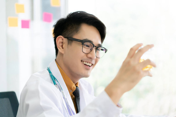 Happy Asian nutritionist doctor showing up a vitamin or nourishment capsules in a bottle close up. Doctor smiling to camera and presenting a vitamin supplement. - Foto, afbeelding