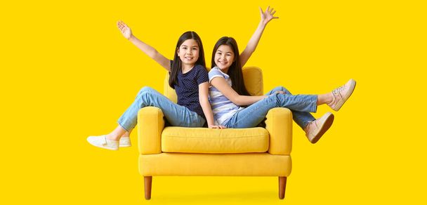 Gelukkig zusjes zitten op fauteuil tegen gele achtergrond - Foto, afbeelding