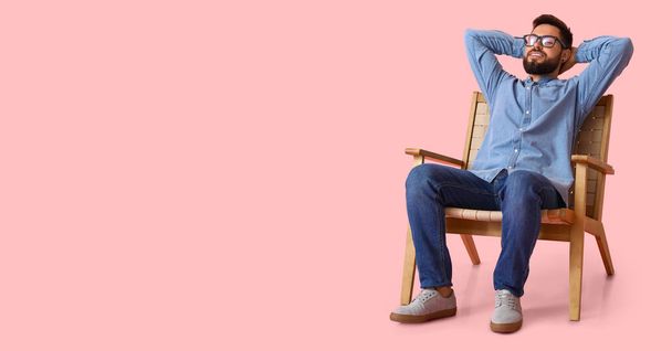 Happy bearded man resting in wooden armchair on pink background with space for text - Photo, Image