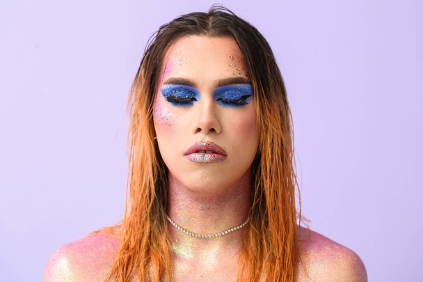 Fashionable young transgender woman with glitters on body against lilac background - Photo, Image