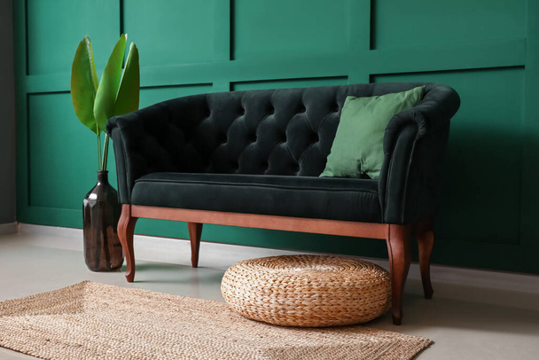 Elegante sofá y jarrón con hojas de palma cerca de la pared verde - Foto, imagen