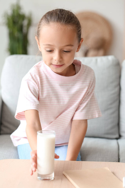 Little girl taking glass of milk from wooden table - Foto, afbeelding