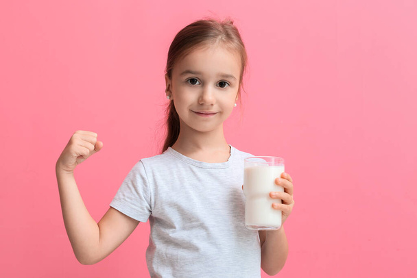 Cute little girl holding glass of milk and showing muscles on color background - Fotografie, Obrázek