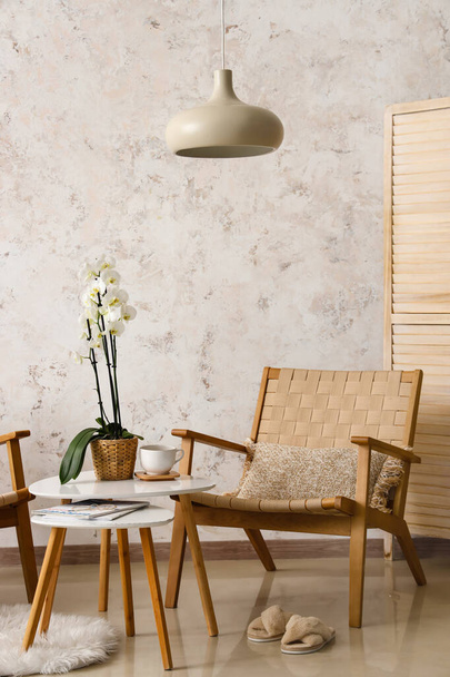 Kényelmes fotel és asztal orchideavirággal a fényfal mellett - Fotó, kép