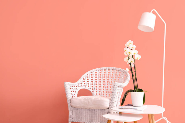 Wicker chair, table with orchid flower and floor lamp near color wall - Fotoğraf, Görsel