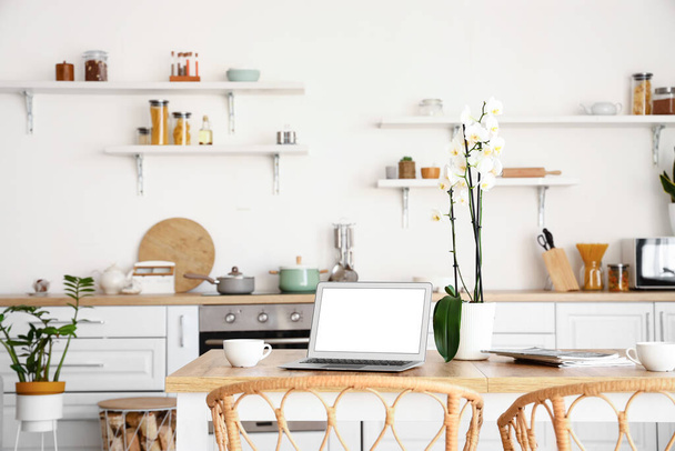 Modern laptop and orchid flower on dining table in kitchen - Foto, imagen
