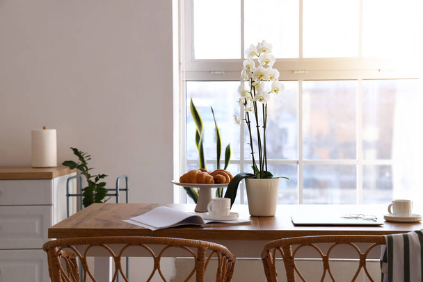 Mesa de comedor con delicioso desayuno, portátil y flor de orquídea en cocina ligera - Foto, Imagen