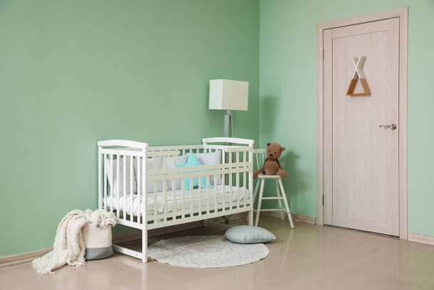 Interior of stylish nursery with baby crib, lamp and chair - Photo, Image
