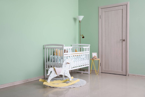 Interior of stylish nursery with baby crib, lamp and rocking horse - Foto, Imagen