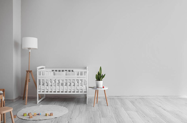 Interior of light nursery with baby crib, lamp and table - Foto, afbeelding