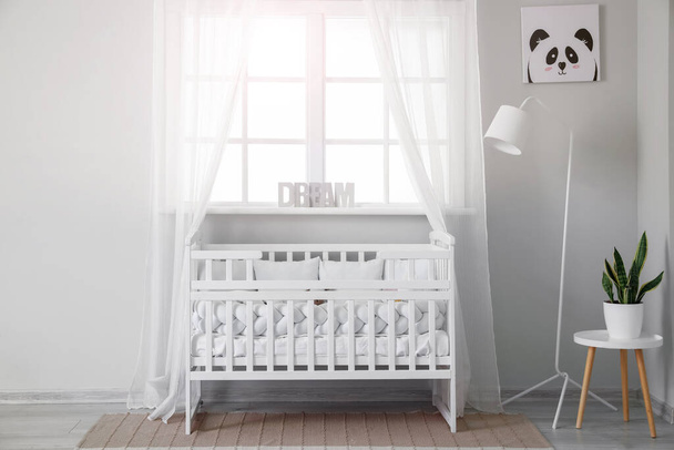 Interior of light nursery with baby crib, lamp and window - Foto, Imagen