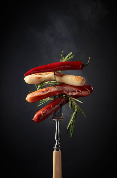 Various hot sausages with rosemary, and hot pepper on a fopk. - Photo, Image