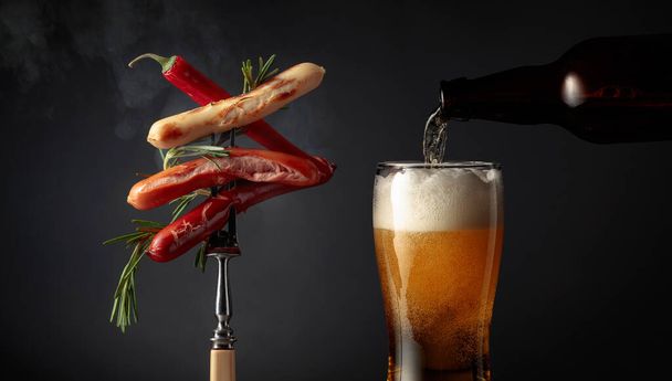 Gorące kiełbaski z rozmarynem, czerwoną papryką i piwem na czarnym tle. - Zdjęcie, obraz