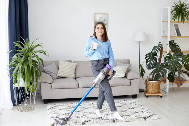 Woman with accumulator vacuum cleaner drinking coffee - Fotó, kép