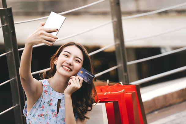 Beautiful smile young asian woman hold smart phone purchase and pay online with credit card. Shopping on holiday sale season concept. City girl lifestyle happy outdoor activity. - 写真・画像