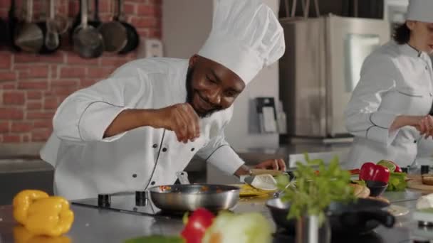 Afrikkalainen amerikkalainen kokki kaataa silputtua juustoa paistinpannulla - Materiaali, video