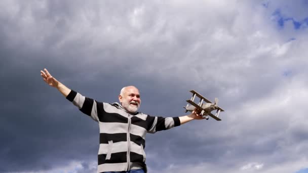 Happy elderly man pretend flying on model aircraft in sky, dream - Footage, Video
