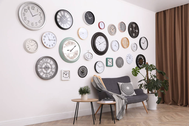 Stylish room interior with comfortable furniture, beautiful houseplant and collection of different clocks on white wall - Foto, Bild