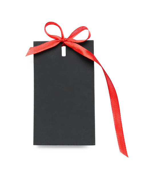 Blank black gift tag with red satin ribbon on white background, top view. Space for design - Foto, imagen