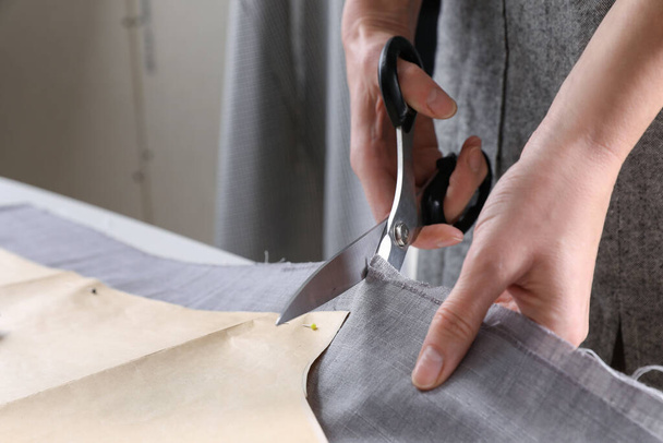 Tailor cutting fabric with scissors at table in atelier, closeup - Fotoğraf, Görsel