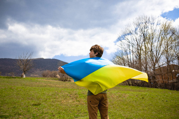 A man holds the Ukrainian flag . Stop war. Against the backdrop of mountains. - Фото, изображение