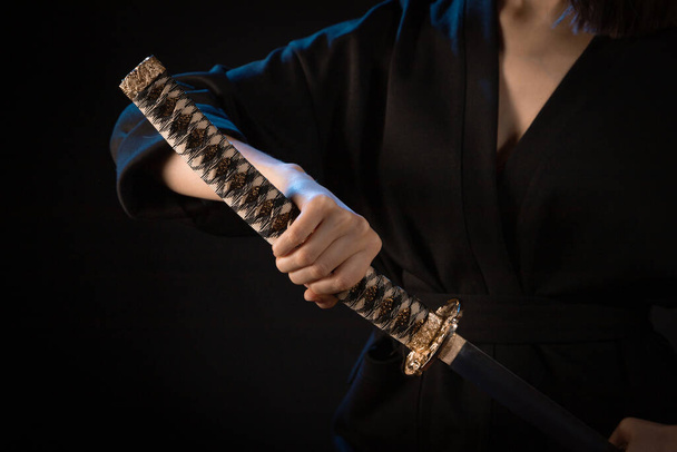 Close-up op het handvat van een Japans zwaard in de hand van een vrouw in een zwarte kimono. - Foto, afbeelding