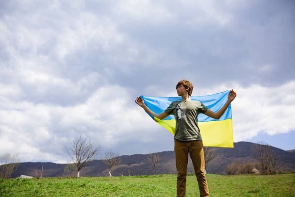 A man holds the Ukrainian flag . Stop war. Against the backdrop of mountains. - 写真・画像