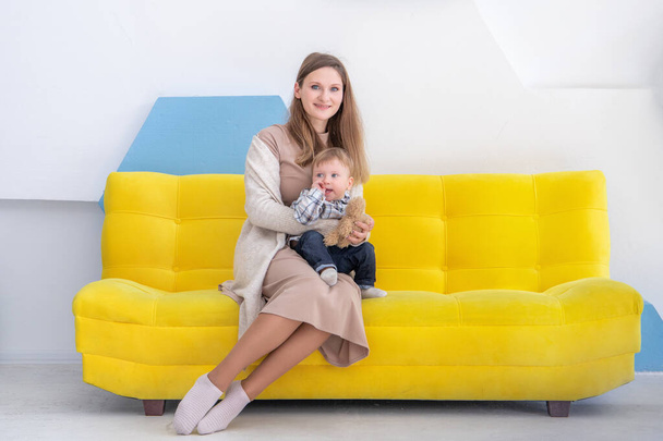 Retrato de una joven europea con un niño pequeño en un sofá en un interior positivo brillante. - Foto, imagen