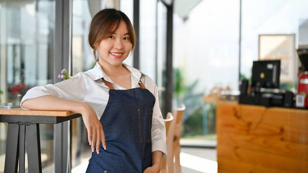 Retrato de una atractiva joven camarera asiática o camarera o dueña de una cafetería de pie en su cafetería mínima. - Foto, imagen