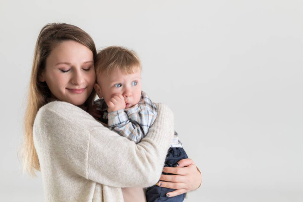 Young happy mother with closed eyes holding baby in hugs on white background - Foto, afbeelding