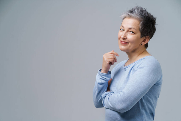 Lovely grey hair mature business woman in 50s posing sideways with hands folded and copy space on right isolated on white background. Copy space and place for product placement. Aged beauty - 写真・画像